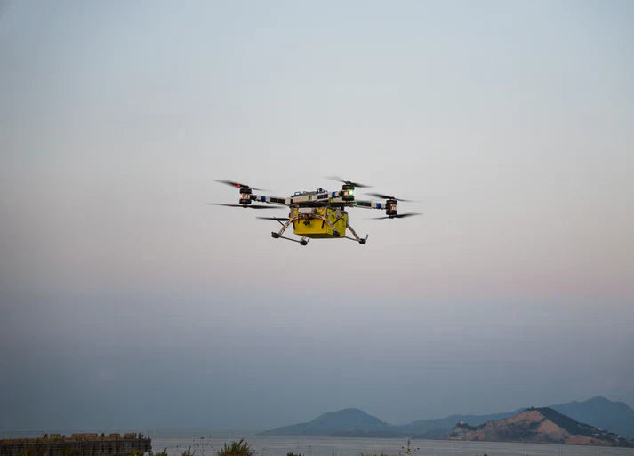 Yellow commercial drone flying outdoors with mountains and water in background, AlphaGeo Ltd