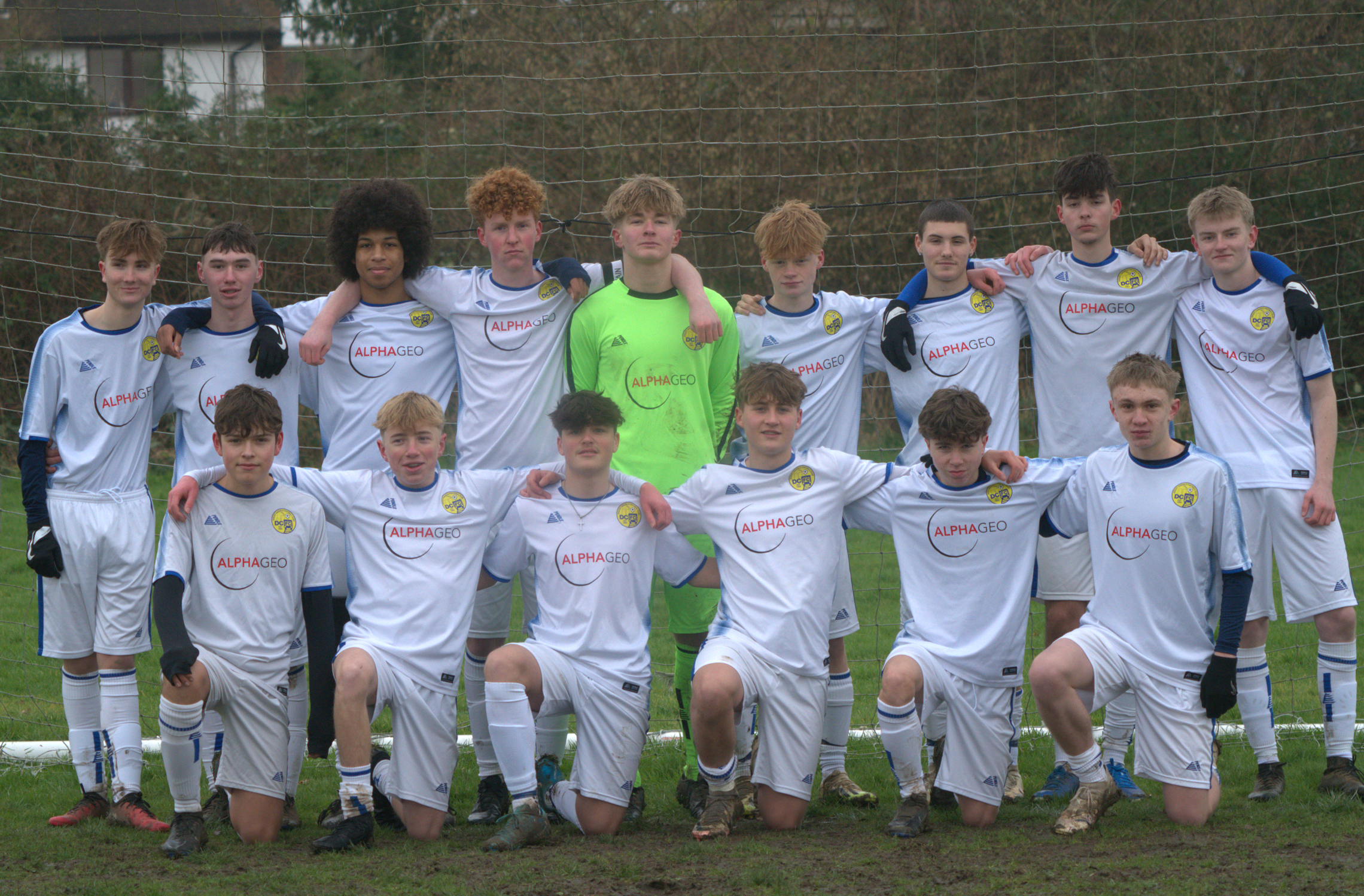 Youth football team in white AlphaGeo-branded kits posing outdoors on a grass pitch