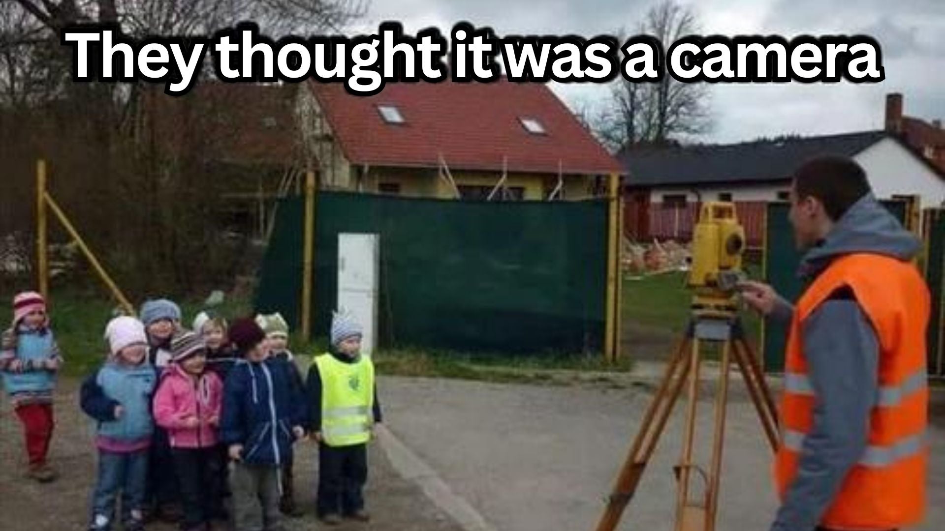 Surveyor with orange vest using total station while kids pose, thinking it's a camera, AlphaGeo context