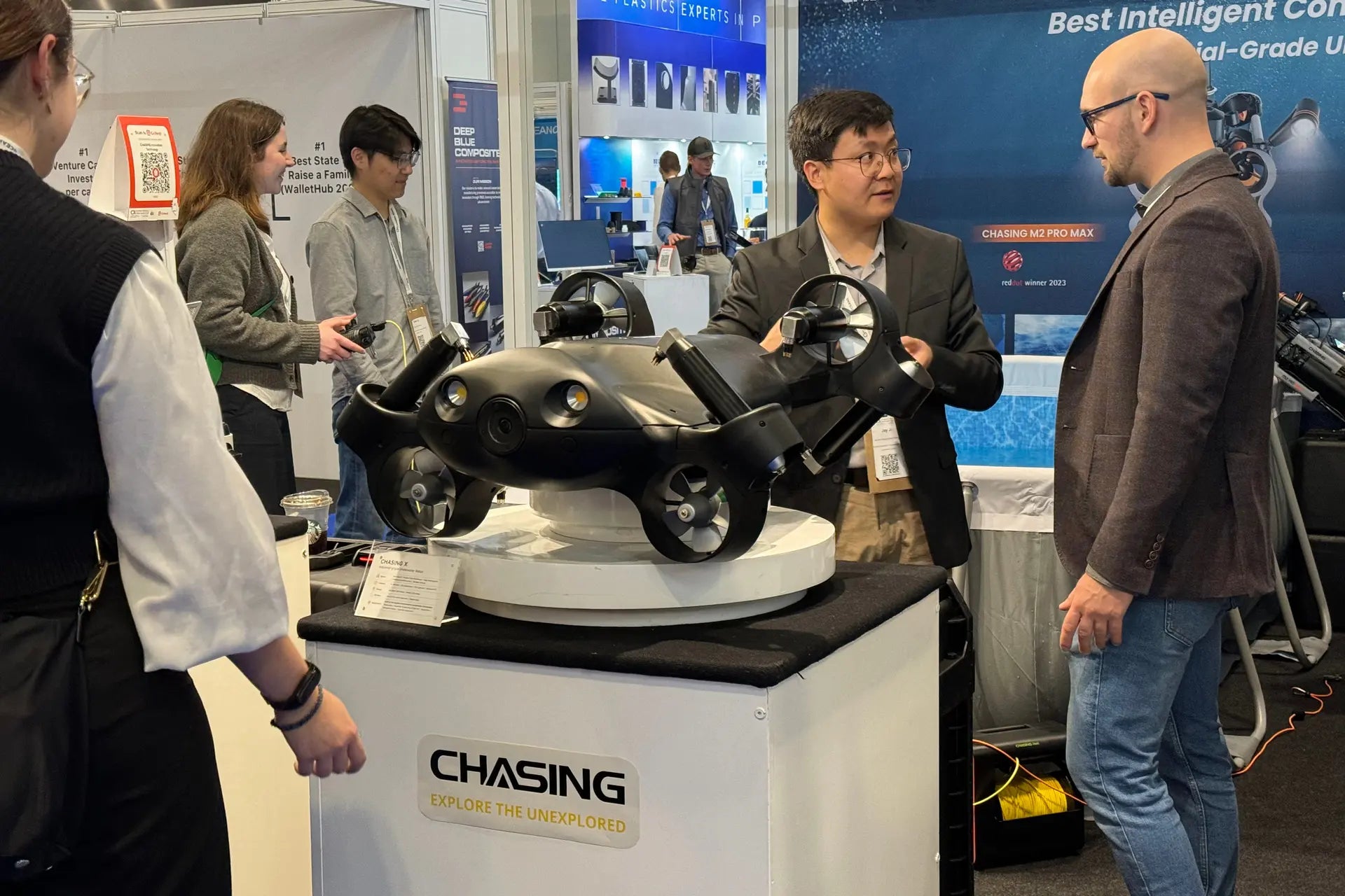 People discussing underwater drone ROV at AlphaGeo Ltd booth with CHASING display